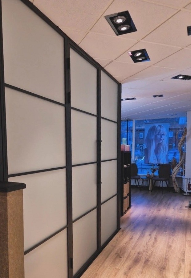 Gang langs een zwart omlijste glazen wand naar de etalage van de salon